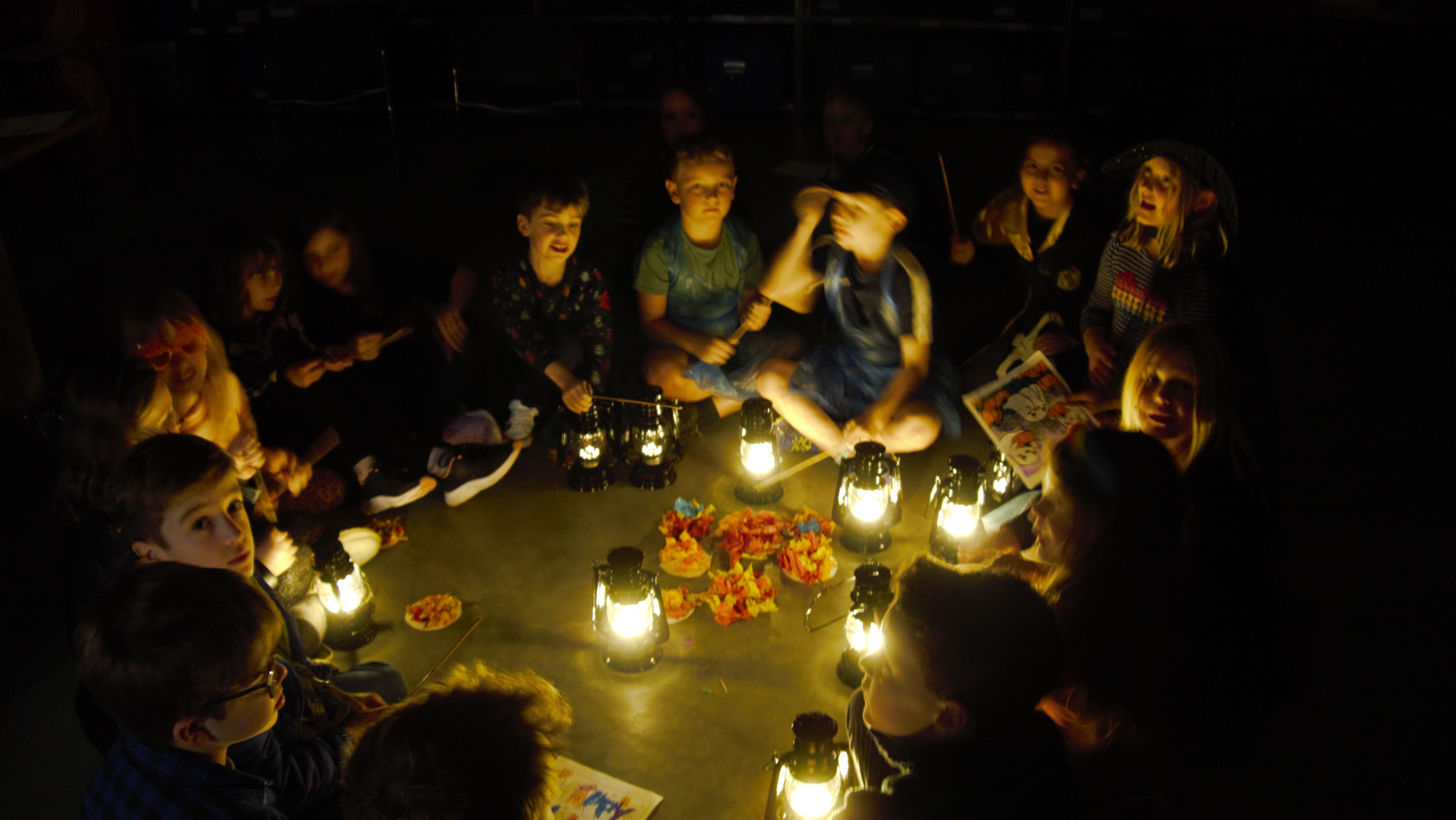 Group of children sat together in a room around lanterns